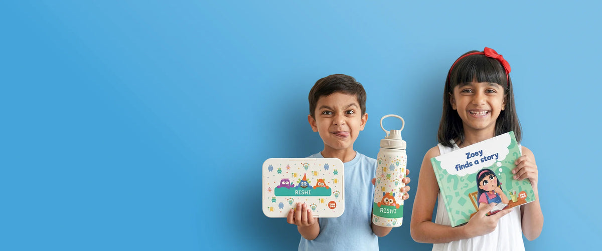 Two children, each holding personalized gifts and school essentials. The boy holds a bento lunch box and an insulated 600ml water bottle. the girl is holding out a personalized storybook