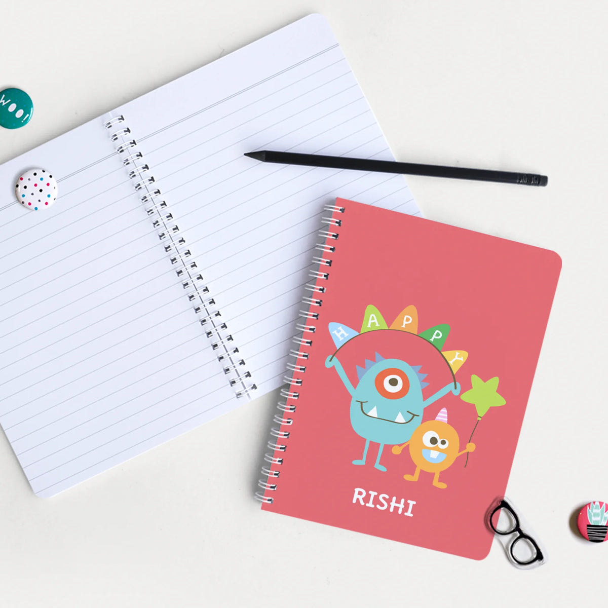 A personalized A5size spiral notebook with cartoon monster illustrations and the name 'RISHI' printed on the cover.