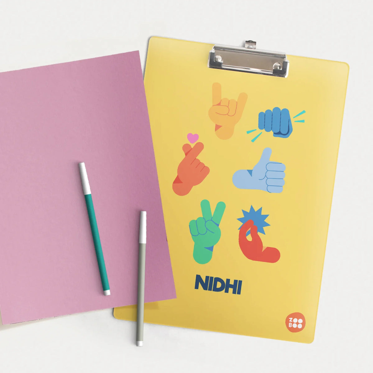 A yellow, sturdy, acrylic, personalized clipboard with a metal clip holds a pastel pink sheet of paper.The clipboard features colorful emoji design.