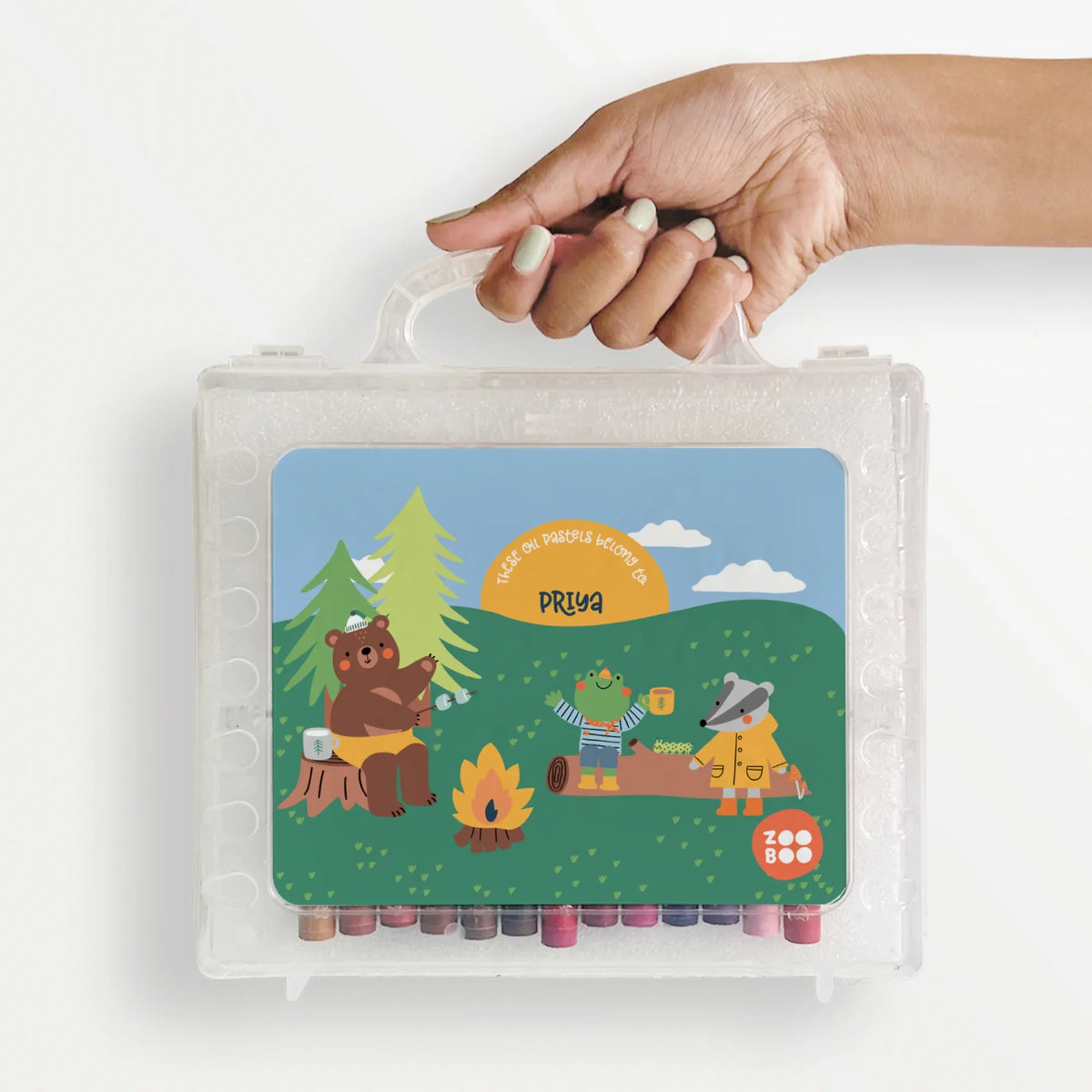 A hand holding a personalized box of50 oil pastels with a camping design.