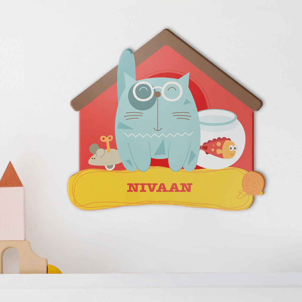 A personalized acrylic plaque, nameboard,  shaped like a house, featuring a light blue cat with glasses, a goldfish in a bowl, a small mouse. The plaque/ nameboard is mounted on a white wall.