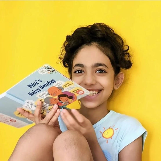 A smiling young girl holding a personalized children's book titled 'Pihu's Noisy Holiday'